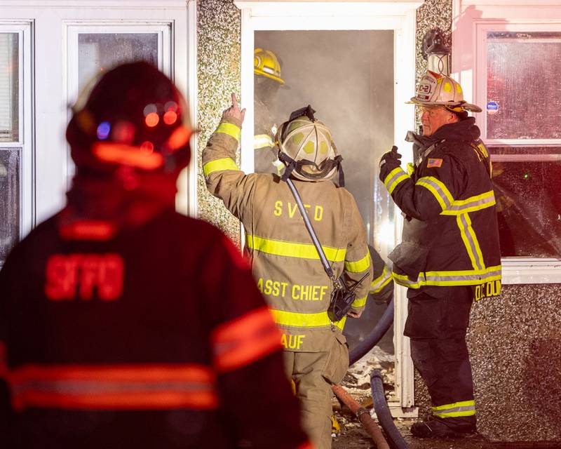 Firefighters standing outside front door of a '2nd Alarm' house fire point towards flame on Saturday, January 10, 2026, at 217 West Delvin Street in Spring Valley.