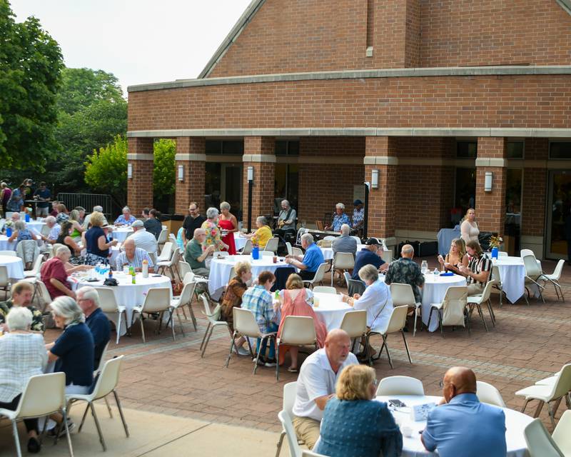 Community members sample food and listen to live music from Mathey Music at Northern Illinois University's Barsema Alumni and Visitors Center on Saturday, Aug. 9, 2025, during CASA DeKalb County's 21st annual Men Who Cook fundraiser before heavy rain made people seek shelter for some time.