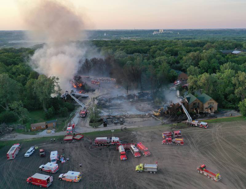Firefighters bring in excavators to help push debris away from flames while fighting a five-alarm fire that burned cabins at the Grand Bear Resort on Monday, May 30, 2022 in Utica.