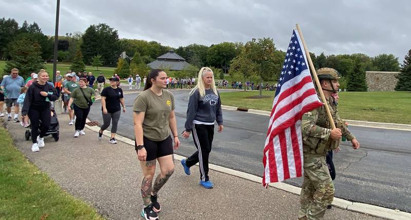 (Right) U.S. Army veteran and reserve member Stephen Cox, 24, of DeKalb, wears his full military garb and hoists an American flag as he joins the line of participants in the inaugural Be the One Walk to raise awareness about veteran suicide rates in DeKalb on Sunday, Sept. 22, 2024. Be the One is part of a national campaign by the American Legion, meant to teach communities how to support veterans' mental wellness.