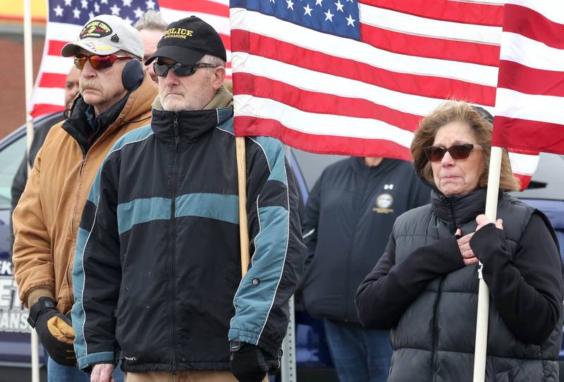 Attendees stand respectfully as the processional honoring DeKalb County Sheriff’s Deputy Christina Musil turns into Butala Funeral Home Monday, April 1, 2024, on DeKalb Avenue in Sycamore. Musil, 35, was killed Thursday while on duty after a truck rear-ended her police vehicle in Waterman.