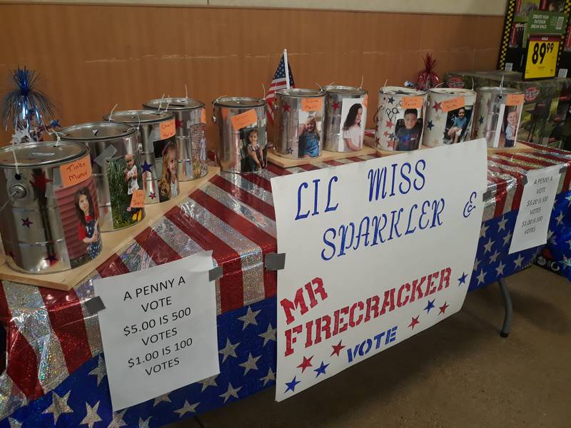 A table is set up at the front of Kroger in Streator with cans to collect votes for Lil Miss Sparkler and Mr. Firecracker. The contest raises money for Streator's 4th of July Celebration.