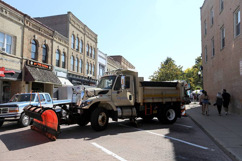 People walk past a dump truck runs with a snowplow blocking off one of the roads leading into the Historic Woodstock Square on Sunday, Sept. 14, 2025, during the annual Hispanic Connections Mexican Independence Day Celebration. The celebration featured music, food and culture.
