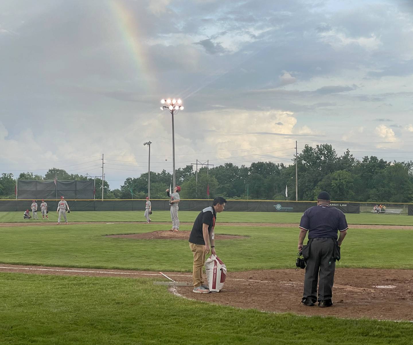 La Salle-Peru athletic director Dan Lee carries a bag of diamond dry compound to home plate as a rainbow appears after a brief downpour during the game between Ottawa and Rock Island in the Class 3A La Salle-Peru Regional on Wednesday, May 25, 2022, at Dickinson Field in Oglesby.