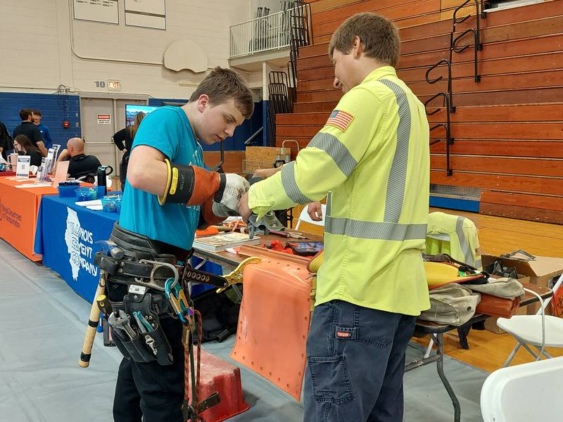 Collin Lund, a sophomore at Princeton High School, tries out lineman gear and tasks Friday, April 19, 2024, at the Corn Belt Energy table during the Career, Job and Volunteer Fair at Princeton High School.