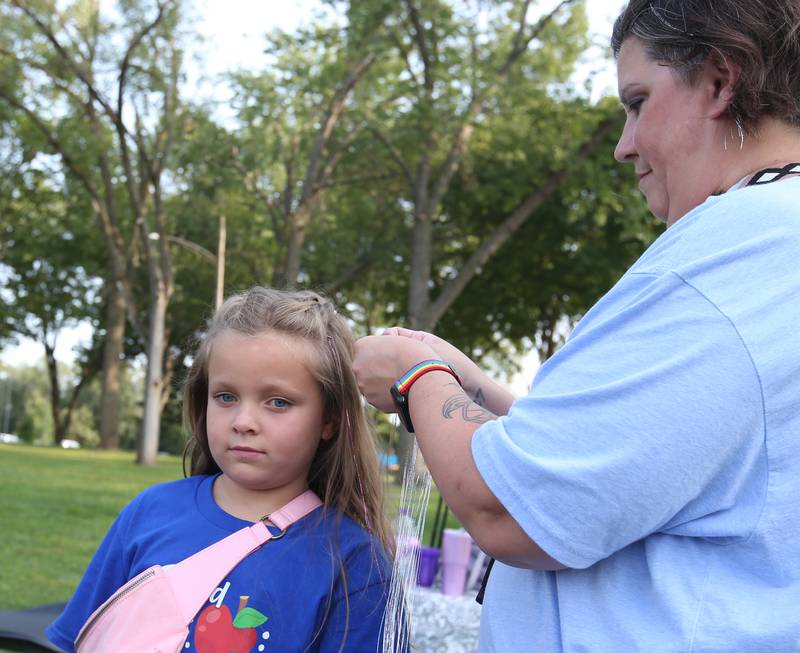 Charlie Piccatto of La Salle, has tinsel applied to her hair by Angie Edgcomb during the Friday Night Market's event on Friday, Aug. 18, 2023 at Kirby Park in Spring Valley. These well-loved markets, traditionally held on the third Friday of each month, moved from the downtown location in the mini park to the captivating and spacious Kirby Park. Fireworks concluded the event.