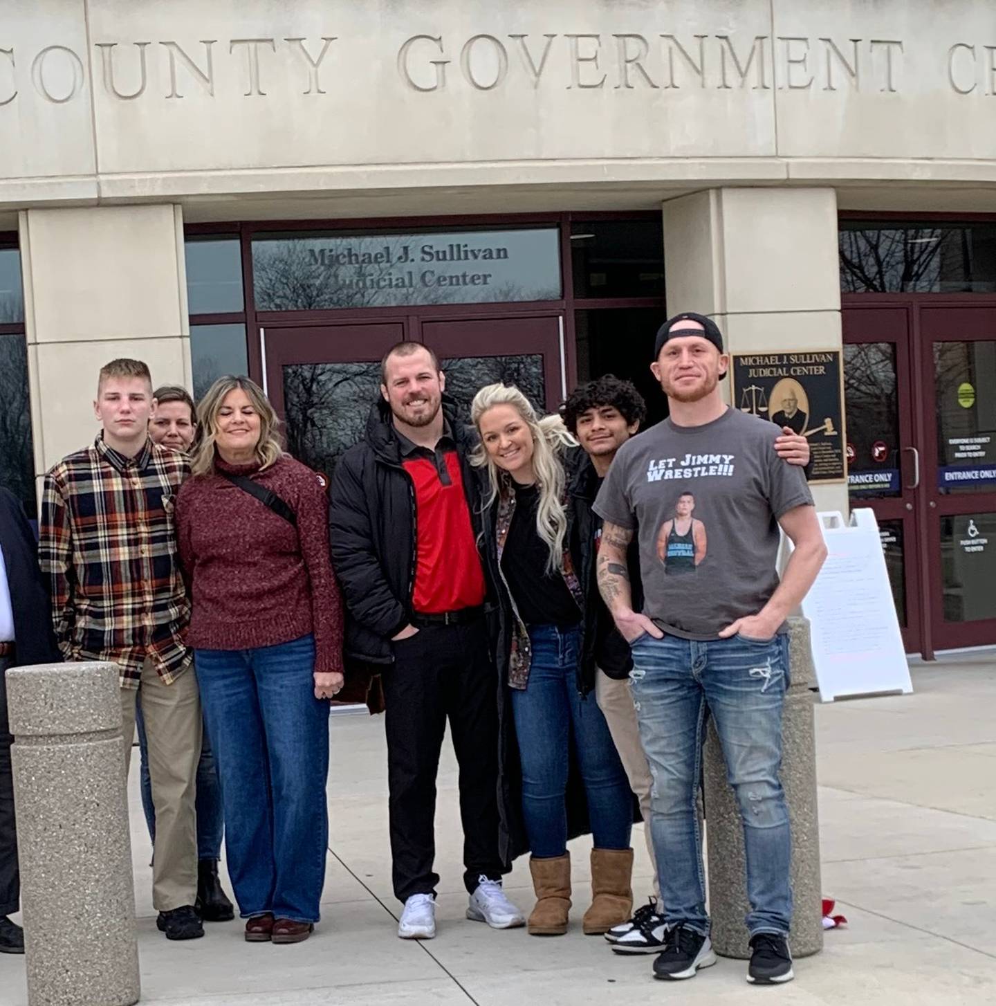 Marian Central Catholic High School student Jimmy Mastny and wrestling co-coach Jordan Blanton and supporters in front of the McHenry County courthouse on Dec. 21, 2023. Mastny and Blanton are seeking an injunction to stop IHSA suspensions. Next to Jimmy is Stacey Blanton, the coach's mother, with whom Jimmy has been staying so he could attend Marian. Behind them is Jimmy's mother, Renee Mastny.