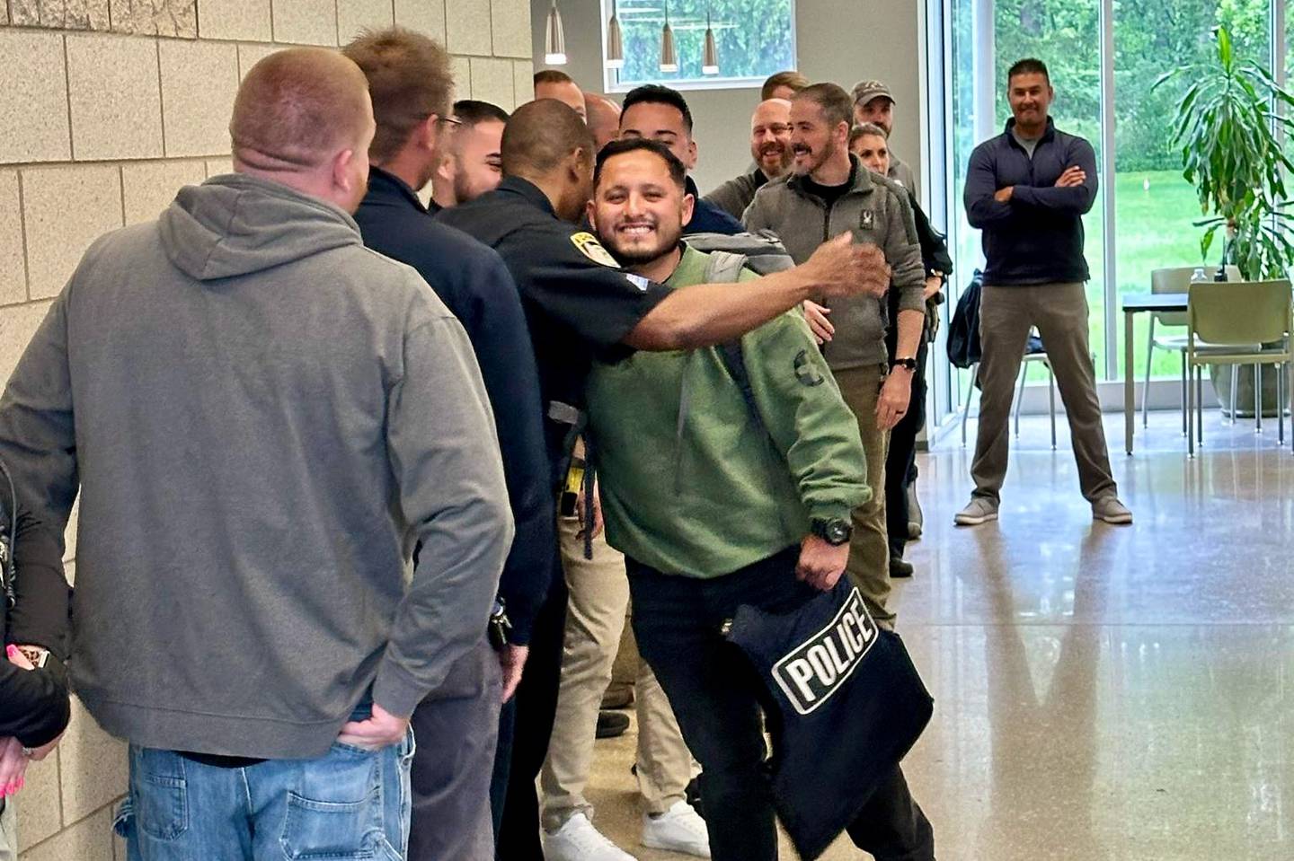 DeKalb police officer Jesus Rodriguez (middle right), embraces colleagues as they line the entrance to the DeKalb Police Department for a warm welcome back on May 28, 2025, following a yearlong U.S. Army deployment to Jordan.