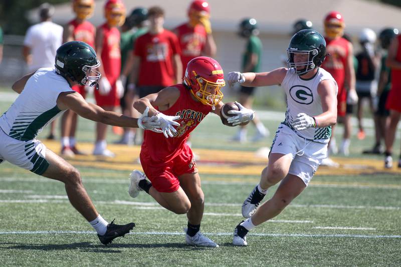 Batavia’s Zach Granberg runs with the ball between a pair of Glenbard West defenders during a 7 on 7 football tournament at Batavia High School on Thursday, July 14, 2022.