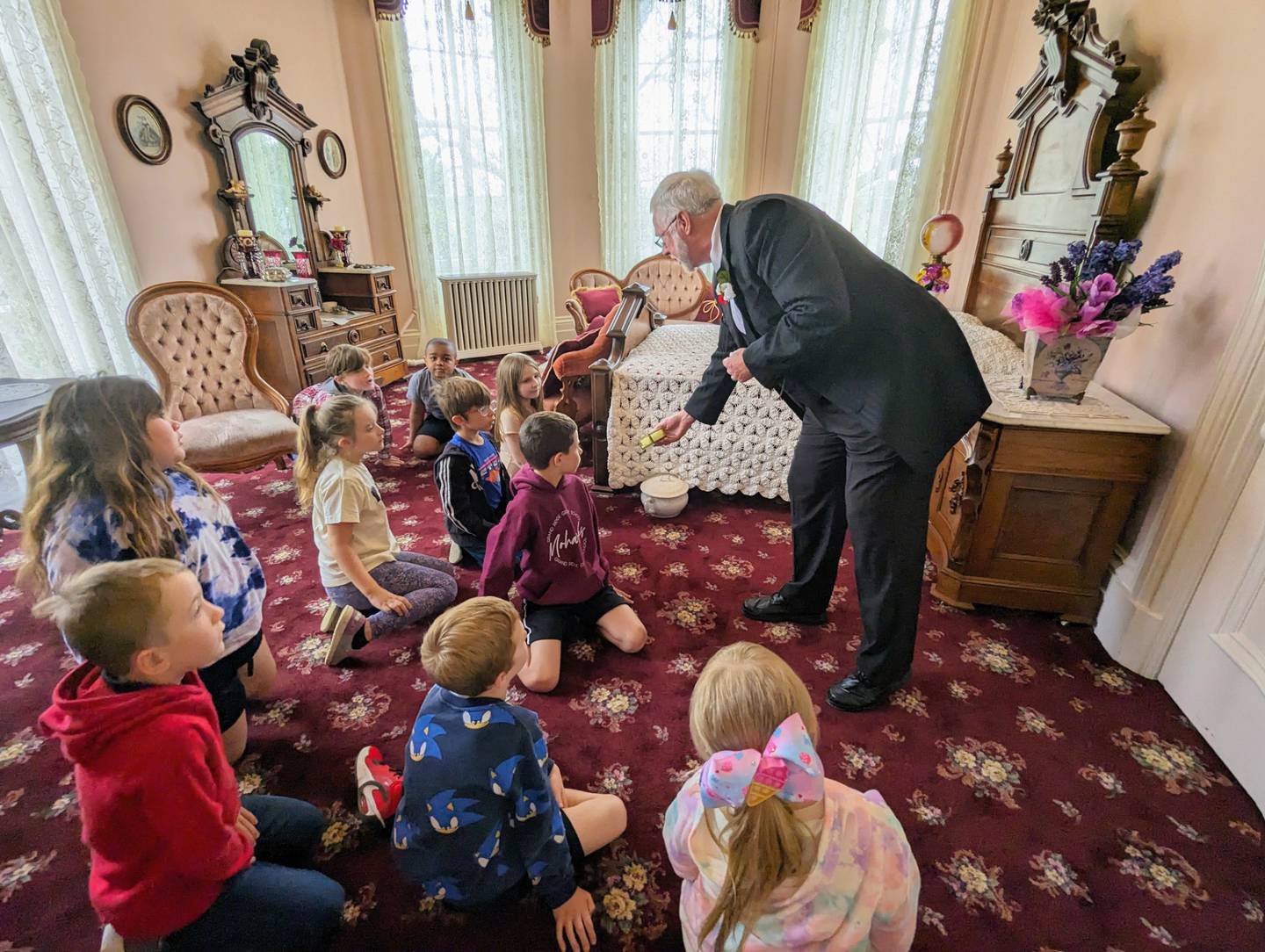 RMA board member Chris McCarter shows students from Grand Ridge the chamber pot near Mrs. Reddick's bed.