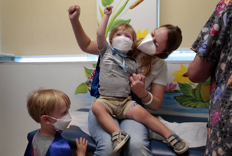 "Give it to the crowd!," yells Jen Maddock as she raises her fist in celebration with son Will, 23 months, after the youngster received his COVID-19 vaccination at Southwest Pediatrics on Wednesday, June 22, 2022, in St. Louis. Will and his brother Jack, 3, waiting his turn at left, wore superhero capes for the occasion. Will was born with a heart defect during the pandemic and his family has remained isolated, with his mother quitting her job. "He hasn't even met all of our family," said Maddock. (Robert Cohen/St. Louis Post-Dispatch via AP)