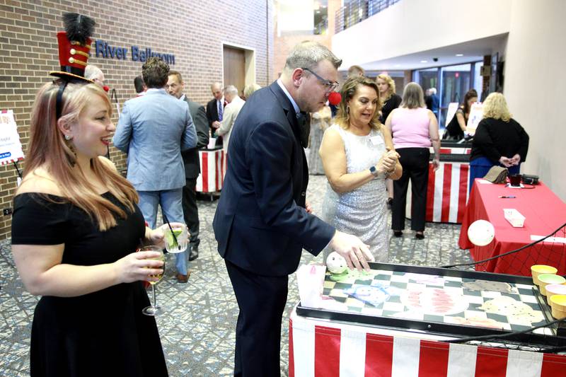 Aubrey Marvel (far left) looks on as Rick Marvel plays carnival games lead by Lori Lain (far right) during the 56th Annual Charlemagne Awards Dinner hosted by the St. Charles Chamber of Commerce at the Q Center in St. Charles on Friday, May 17, 2024.