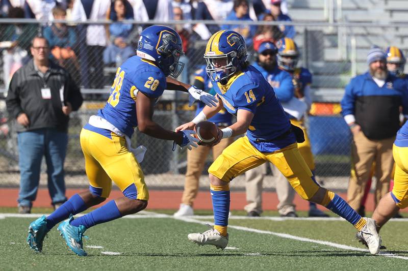 Joliet Central’s John Stasiak hands the ball off to Marcus Hill against Joliet West in the cross town rival matchup on Saturday.