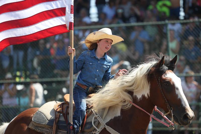 A girl rides with the American flag before the start of I.P.R.A. World Championship Rodeo the at the Will County Fair on Sunday, August 25, 2024 in Peotone.