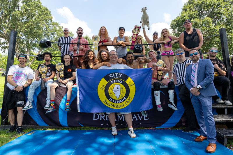 (front, center) Peru Mayor Ken Kolowski holds 'City of Peru' flag as DreamWave Wrestlers pose for photo in front of ring at the Taste of the Illinois Valley DreamWave Wrestling event on Saturday, August 2, 2025 at Centennial Park in Peru.