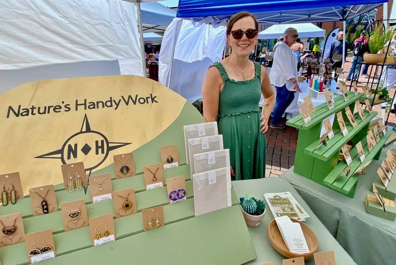 Tori Eisenberg poses with at her vendor booth for her business Nature's HandyWork during the opening day of the DeKalb farmers market on Thursday, June 5, 2025, in Van Buer Plaza in downtown DeKalb. Eisenberg forages for flowers, plants and other items near her home along the Fox River to make jewelry, bookmarks and other goods.