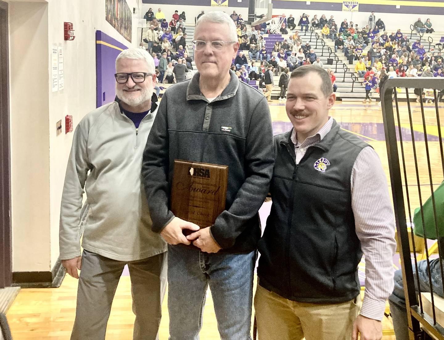 Mendota principal Joe Masini (left) and Athletic Director Brock Zinker (right) presented Kip Cheek of the Mendota Reporter with the IHSA Most Distinguished Media Award, on behalf of Matt Troha of the IHSA, prior to Tuesday's varsity game with Rock Falls. Cheek has covered Mendota sports for 40-plus years, arriving in May of 1984