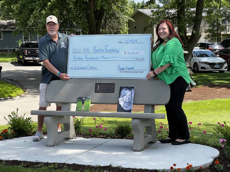Roger Finnan and Angela McCrum hold an symbolic check above a bench dedicated to Shannon Finnan, at the River Heights Golf Course in DeKalb on July 19, 2024.
