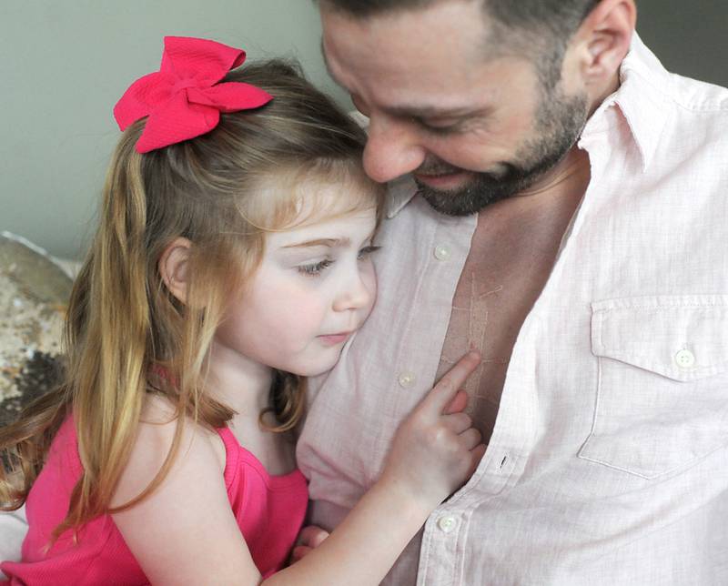 Everly Backe, 4, who has had multiple open heart surgeries to correct congenital heart defects, looks at her dad’s new tattoo Friday, Feb. 11, 2022. As Everly has became more aware of her chest scar, which they call her "zipper," her dad, Matt Backe, recently decided to get a tattoo that matches his daughter's scar from her surgeries so she does not feel alone in having the scar.