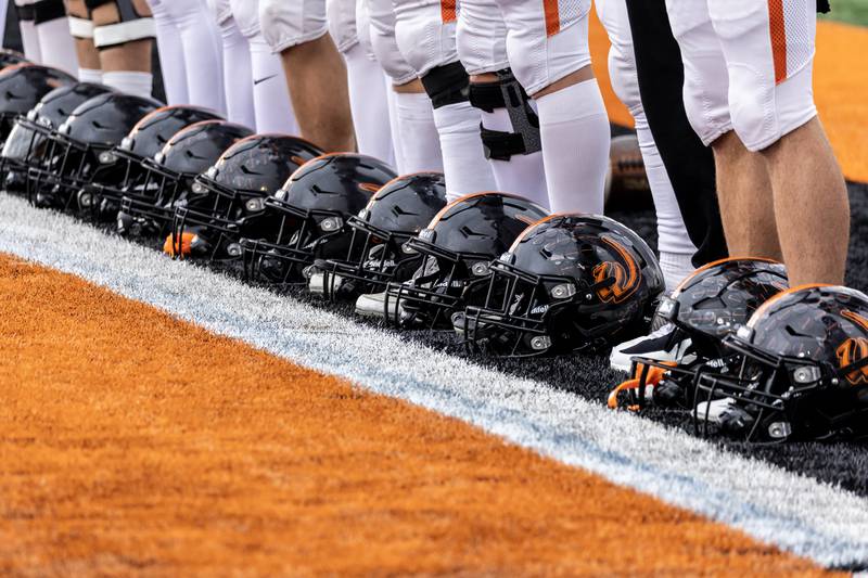 Lincoln-Way West’s helmets rest at player’s feet as the National Anthem plays prior to a 7A varsity football playoff game against Kenwood at Lincoln-Way West on Nov. 8, 2025.