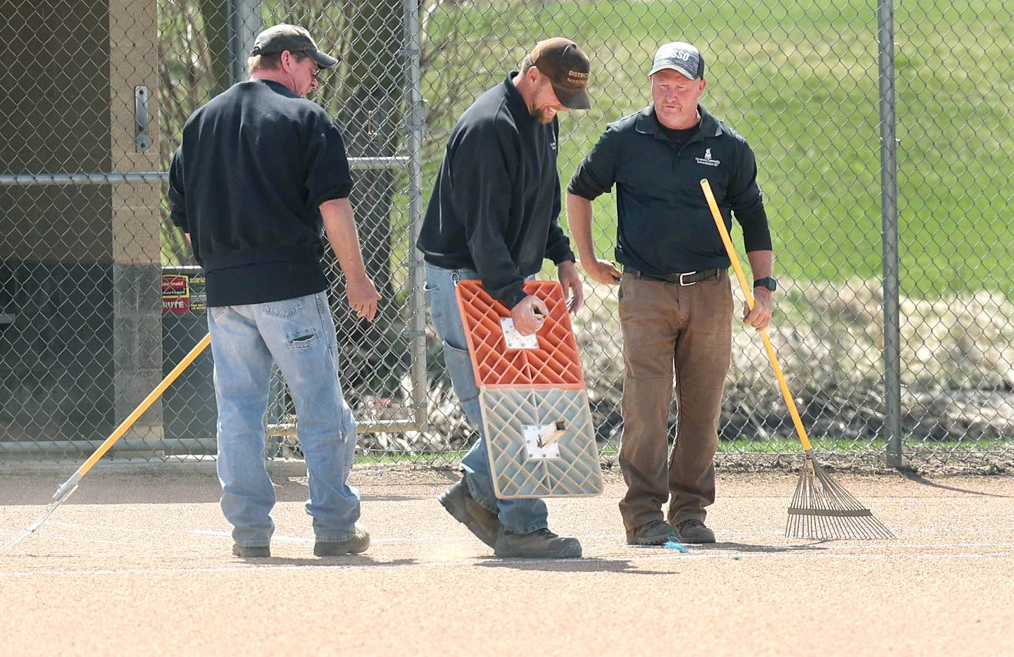 Dane Shaw (left) and Nik Vinz, both maintenance for Sycamore Community School District 427, along with Tom Pritchett, (right) head grounds keeper for the district, put in first base as they get the softball field ready for a game Tuesday, April 11, 2023, at Sycamore High School.