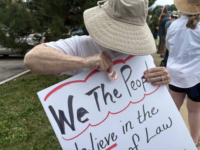 Barbara Roth places an anti-Trump sticker on her sign at a protest in McHenry July 26, 2025.