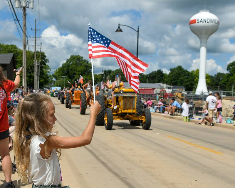 Lily Gugh, 7, of Sandwich waves an American flag as a line of tractors pass by during the Freedom Parade in downtown Sandwich on Saturday July 6, 2024.