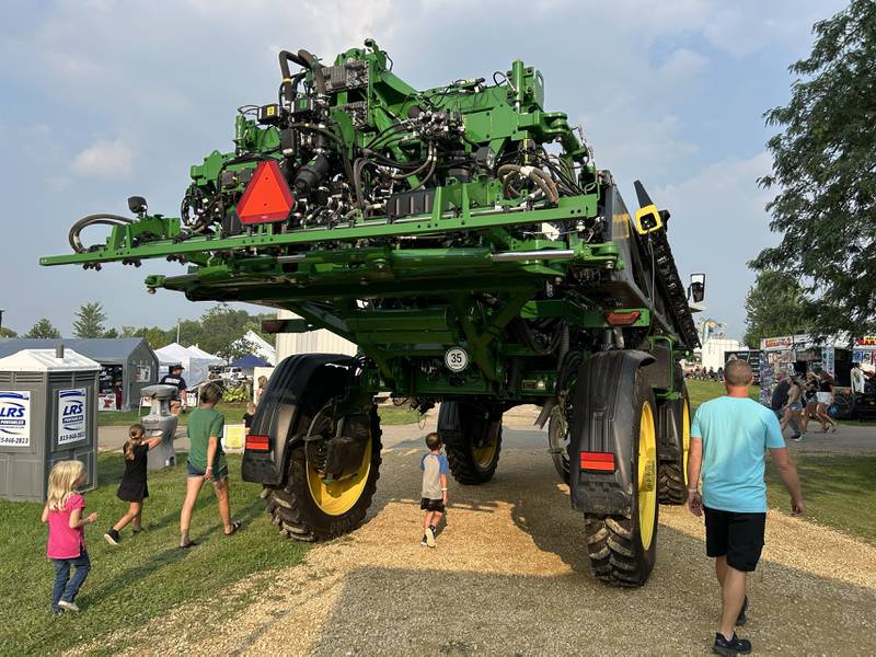 A family walks by and under one of the large pieces of farm machinery that was on display at the Ogle County Fair in Oregon on Thursday, July 31, 2025.