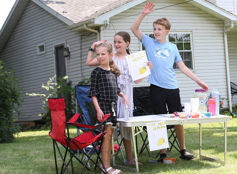 Millicent Fegovich, and her friends Greta and Gavin Conry wave down a motorist as they sell homemade lemonade in the Clarks Hill neighborhood on Monday, July 15, 2024 near Utica. With temperatures in the 90's, the trio decided to set up a lemonade stand for passerbys to patronize.