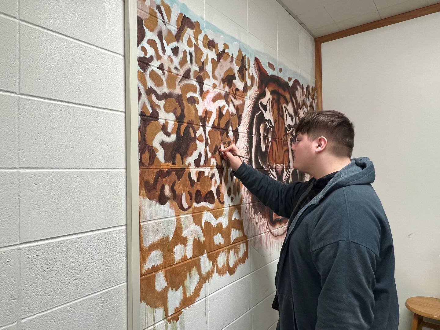 Justin Matlow, 15 and a sophomore at Joliet West High School, is freehandedly creating a tiger mural in English/journalism Jenn Galloy's classroom to serve as a backdrop for her students' regular Tiger News broadcast.