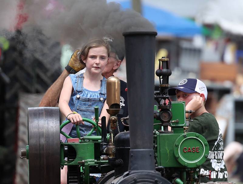 Evalynn Chapman, 8, from Oregon, steers a Case half scale steam engine through the parade with a little help from her grandpa Dave Stevens, from Sycamore, Thursday, Aug. 7, 2025, at the 68th annual Sycamore Steam Show and Threshing Bee at Taylor Marshall Farm on Lukens Road in Sycamore.