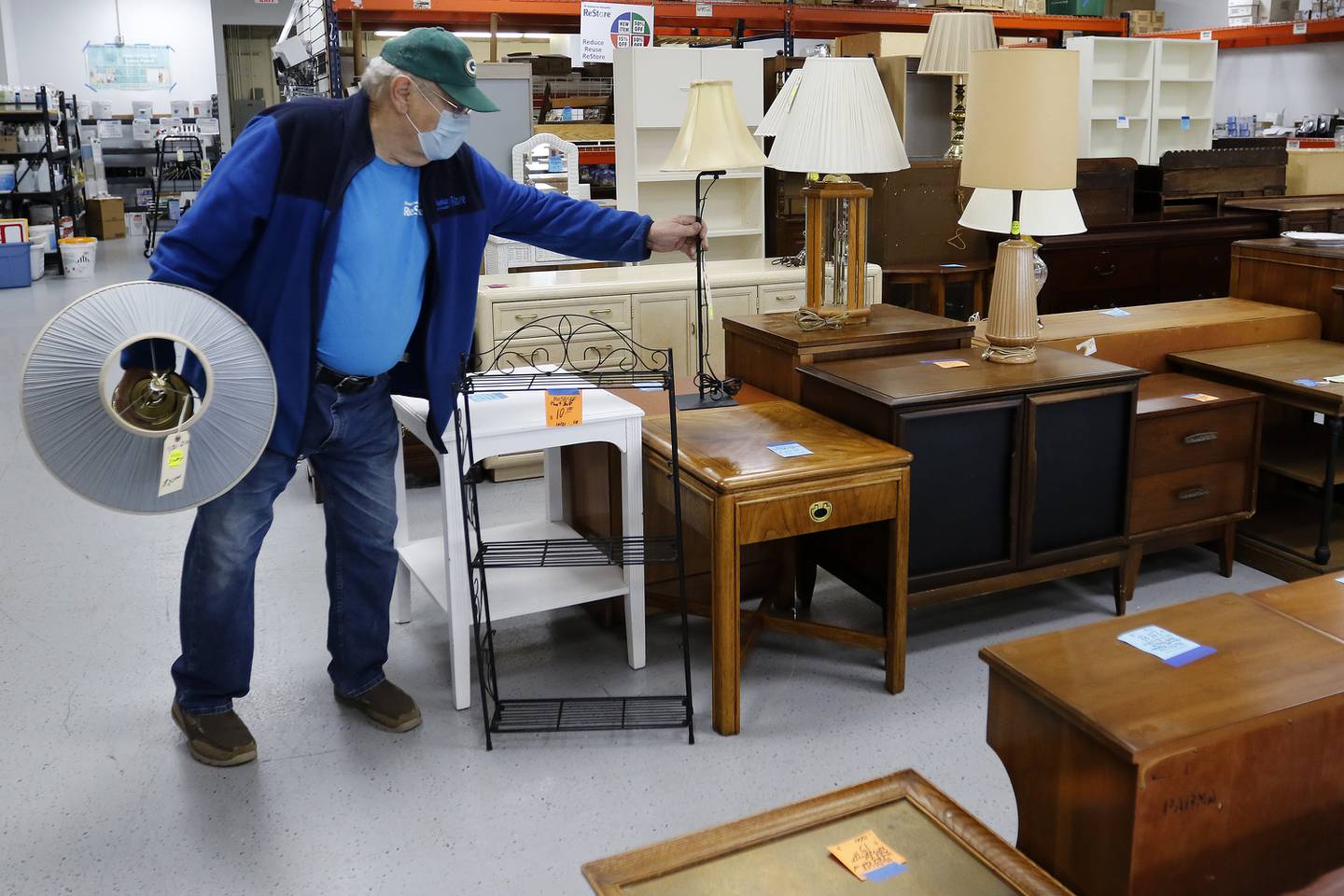 Warren Wascher puts lamps out for sale after testing them for functionality Thursday, Nov. 18, 2021, at the Habitat for Humanity ReStore location in Woodstock.  A backlog of supplies at many retail furniture and home decor stores has contributed to an increase in shoppers purchasing their home furnishings from antique, thrift, and secondhand stores.