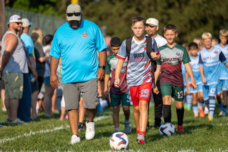 (from left) Coach Salvador walks with Lucas Vanwiggeren at the opening day ceremony of youth soccer on Saturday, Aug 16, 2025, at Peck Park in Ottawa.