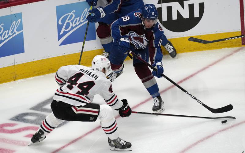 Colorado Avalanche center Alex Newhook, back, passes the puck as Chicago Blackhawks defenseman Calvin de Haan covers in the first period of an NHL hockey game Wednesday, Oct. 13, 2021, in Denver.