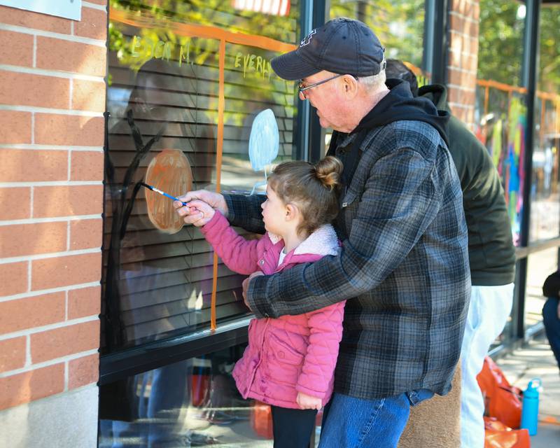Gary Marin Helps his granddaughter Eden Mitchell, 3 years old, both from Downers Grove paint a window during the Halloween Window painting event held downtown Downers Grpve on Saturday Oct21, 2023.