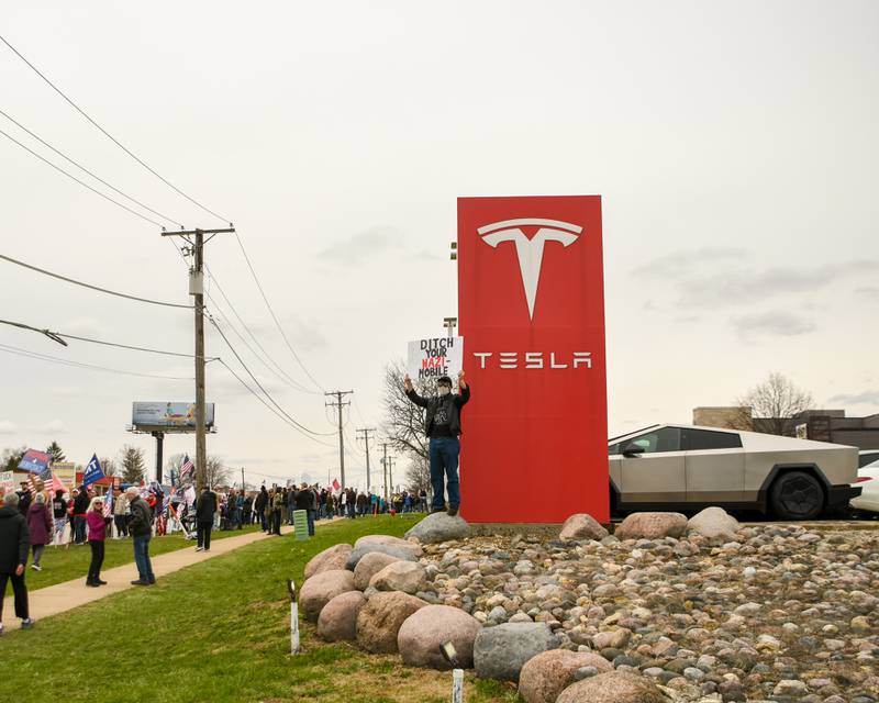 A Community member holds a sign along Ogden Ave. outside of the Tesla dealership on Saturday April 5, 2025, in Lisle during the Hands Off Demonstration.