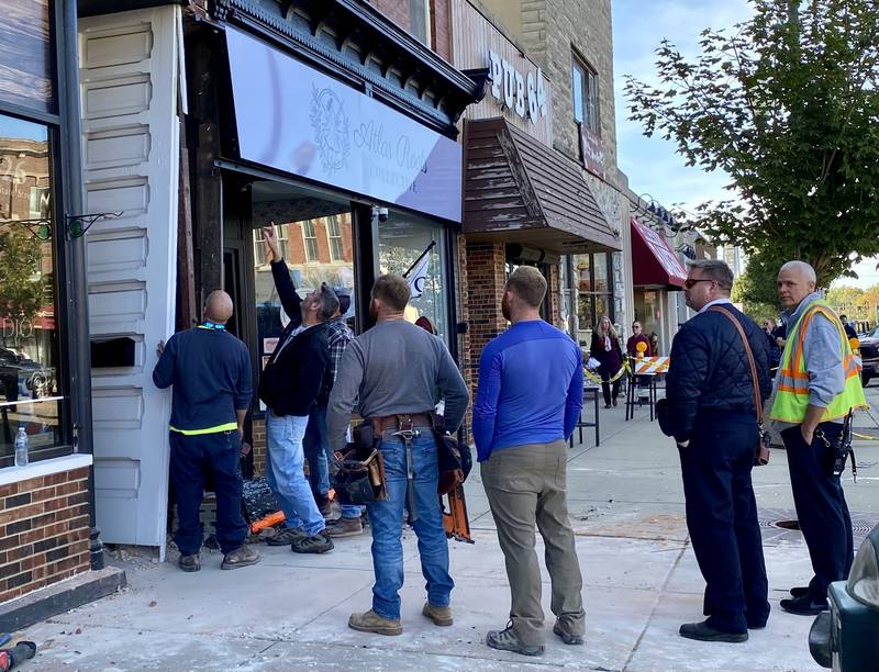 Sycamore city building inspectors, firefighters and police, including Fire Chief Bart Gilmore (second from right) watch as authorities review damage caused to the front of Atlas Roots Collective women's clothing store at 330 W. State St. in downtown Sycamore on Friday, Oct. 24, 2025. Police said a vehicle crashed into the front of the store, injuring a driver and a passenger.
