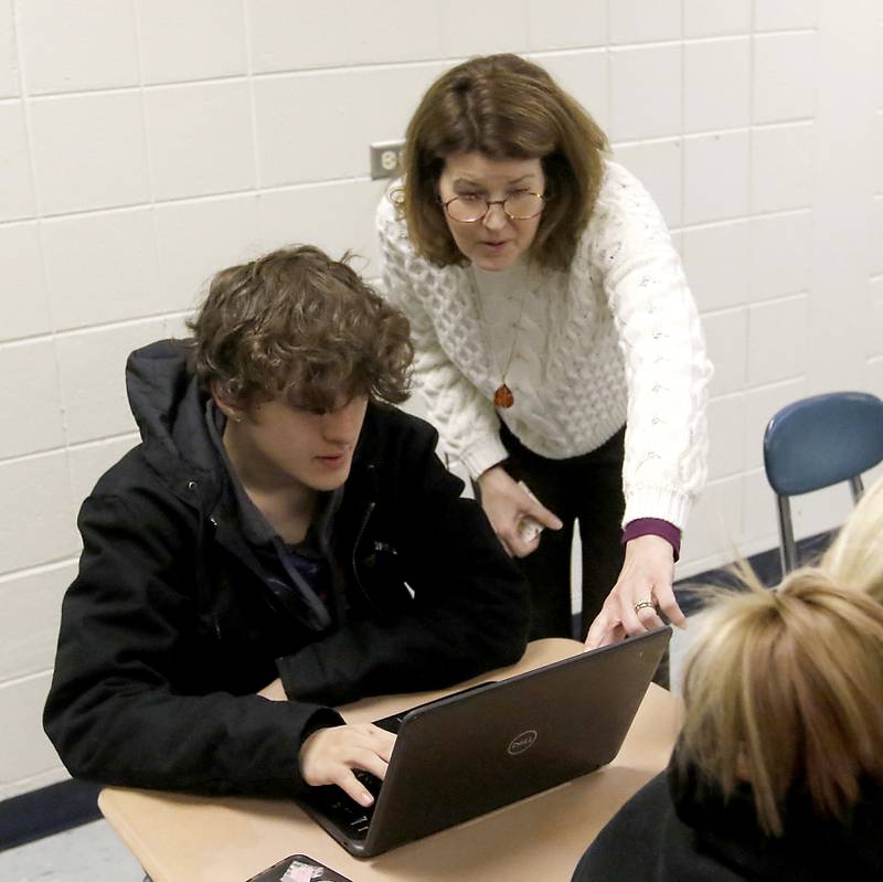 Teacher Christine Keogh-Baker helps senior Christian Olson with a writing assignment during a dual credit composition class Wednesday, March 1, 2023, at Woodstock High School.