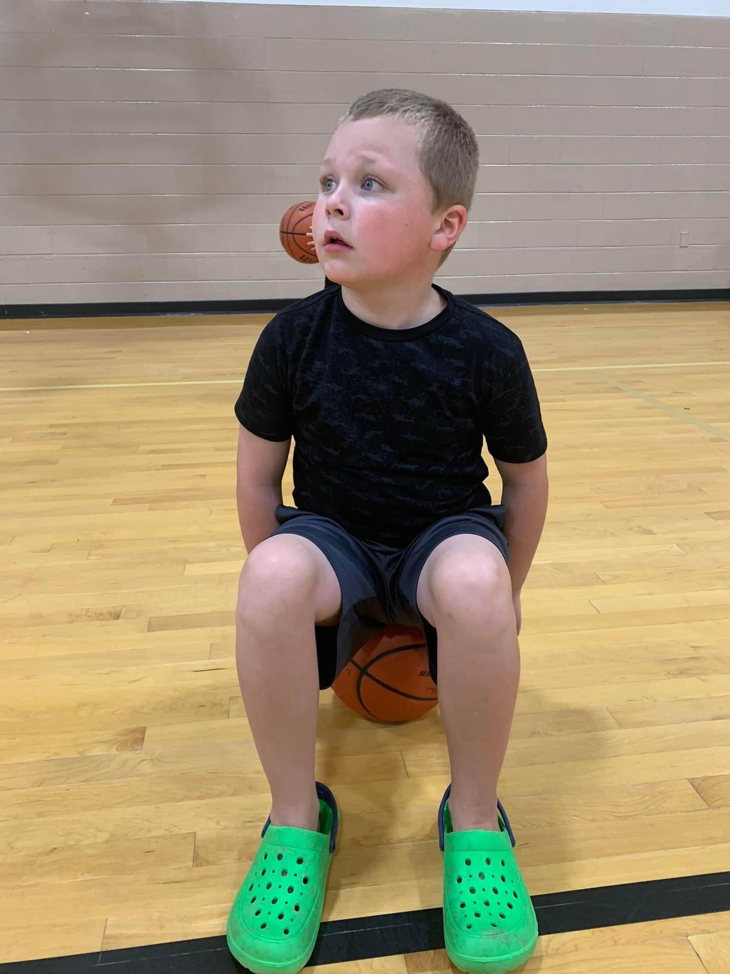 Alan Maziur, 7, and son of Jenna Maziur, a girls basketball coach at Providence Catholic High School in New Lenox, sits on a basketball during a basketball camp at the school in the summer of 2022. Alan has nonverbal autism and loves basketball. He will participate in a basketball camp for students with special needs in January 2023. Jenna will help run it.