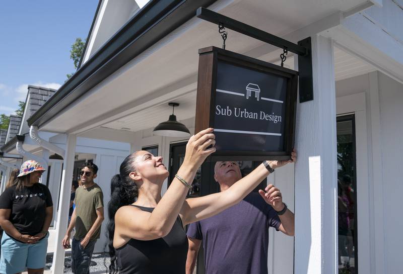 Store owner Kristina Dillard along with husband, Nick, hang the sign for their tiny shop, Sub Urban Design, during the grand opening and ribbon cutting of the new McHenry Riverwalk Shoppes in downtown McHenry on Friday, July 21, 2023.