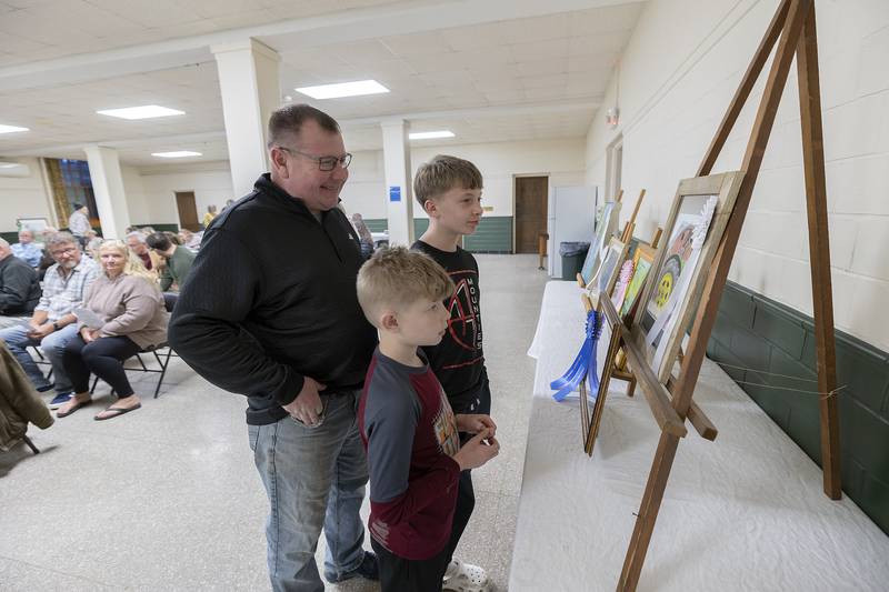Jason Lilly with sons Camden, 9, and Parker, 13, looks over mom Brandi Benson’s award winning work Thursday, April 3, 2025, at the Phidian art show.