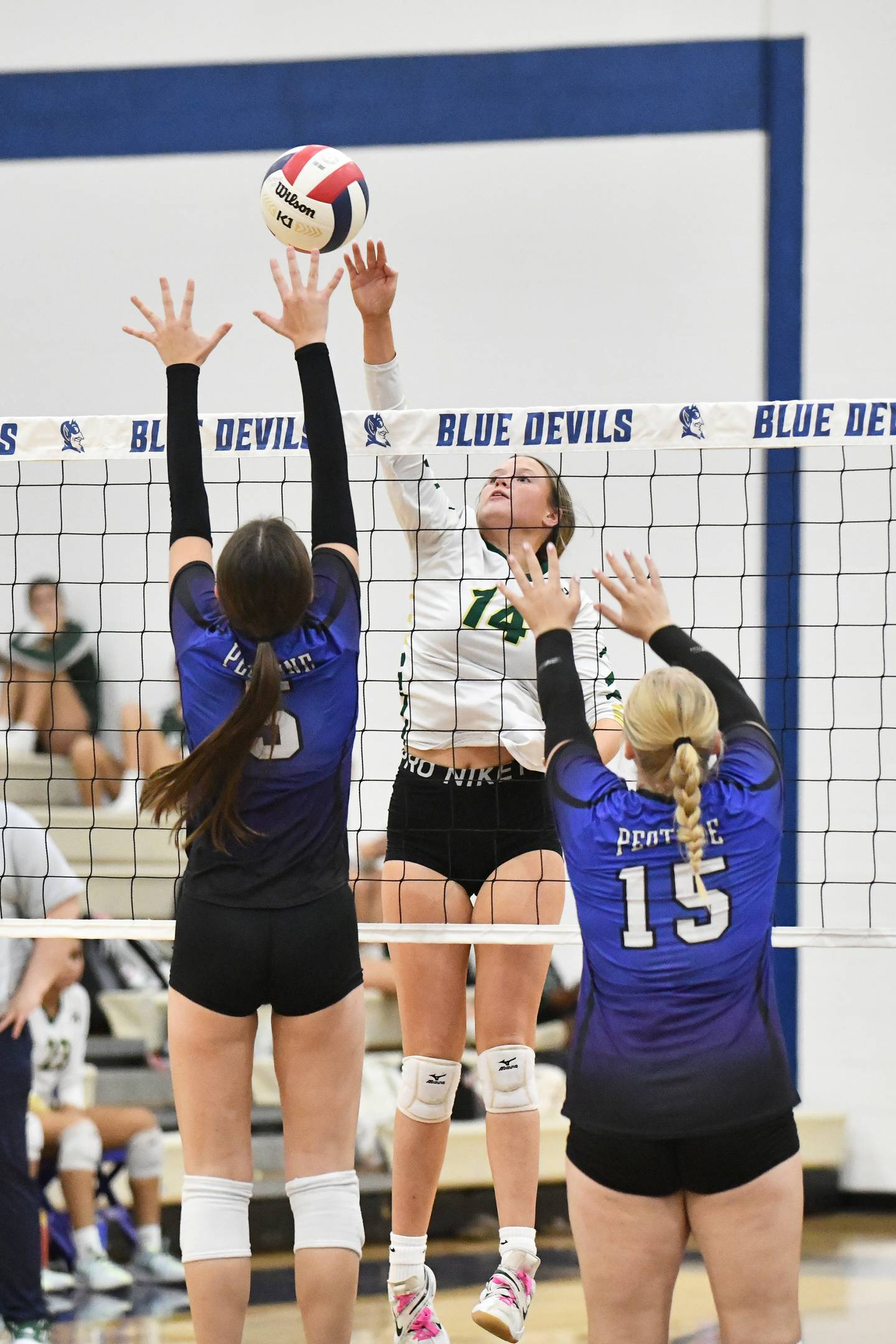 Bishop McNamara's Kate Dole hits the ball over a block by Peotone's Cora Pagliarulo, left, and Jersey Slone during the Blue Devils' victory in three sets, 25-17, 22-25, 26-24, over Bishop McNamara on Sept. 23, 2024.