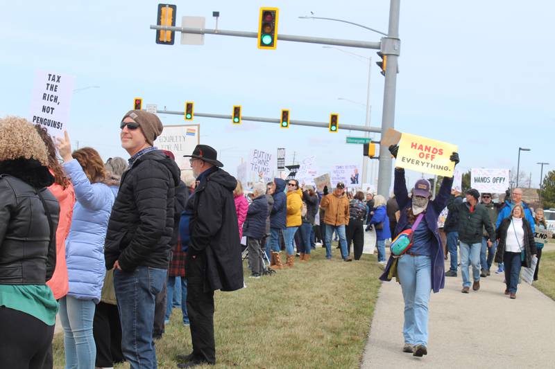 A woman holds up a sign reading "Hands up everything" during the "Hands Off" protest along Randall Road in Algonquin on April 5, 2025.