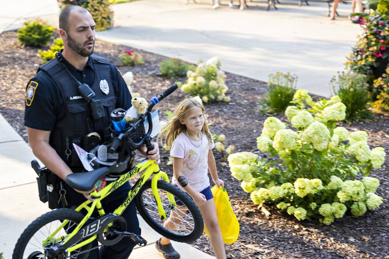 Sterling officer Lucas Nease carries Delylah Celestino’s, 7, new bike for her Tuesday, August 5, 2025, after the young lady won a raffle at National Night Out. The department gave away four bikes during the celebration.