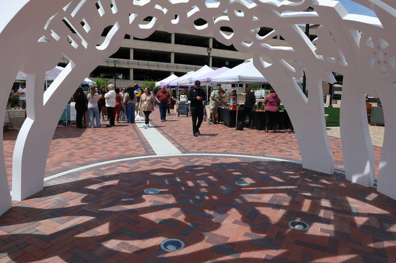 The new sculpture sits in the foreground at the new city square during the farmers market on Friday, May 22, 2026 in Joliet.