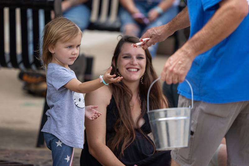 (left) Ellia Williams is handed candy by Mike Phillips as (center) mother Emily watches with smile on Sunday, Aug 31, 2025 at the Labor Day parade on Main Street in Streator.
