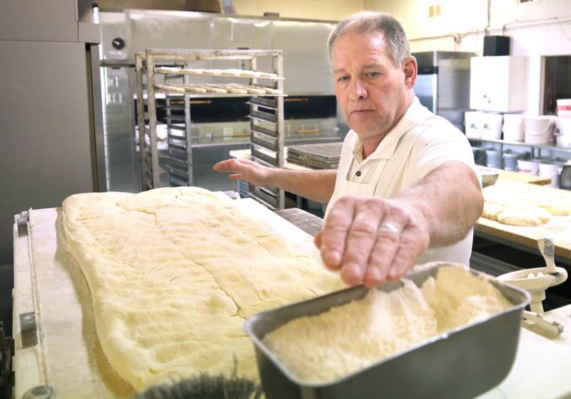 Ken Elleson, owner of Elleson's Bakery, applies flower to the dough before it is sliced up for paczkis Monday, Feb. 28, 2022, in the kitchen of the bakery in Sycamore. Elleson and members of his family will be working all night making the paczkis from scratch to be ready at 5 a.m. tomorrow for Fat Tuesday.