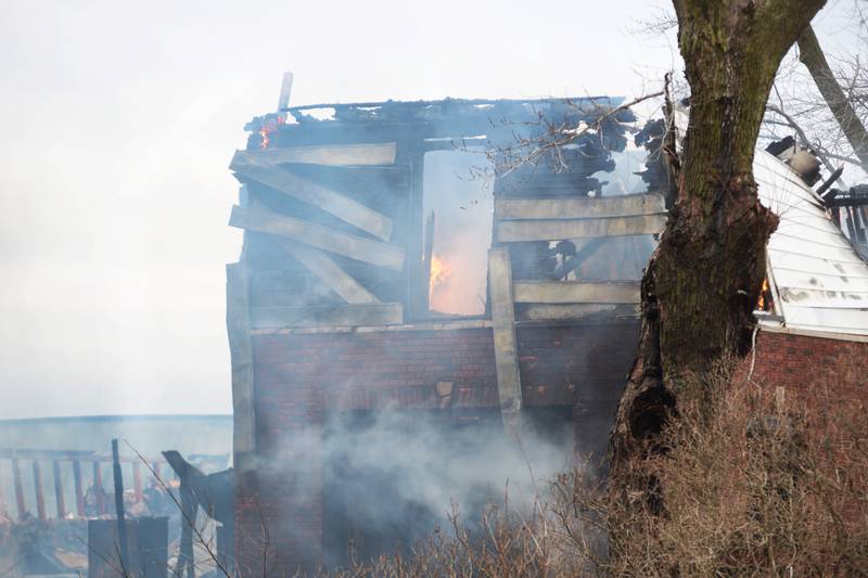 Flames appear through an upstairs window as firefighters spray water on a two-story house at 8423 East Illinois route 38 on the afternoon of Wednesday, March 5, 2025.