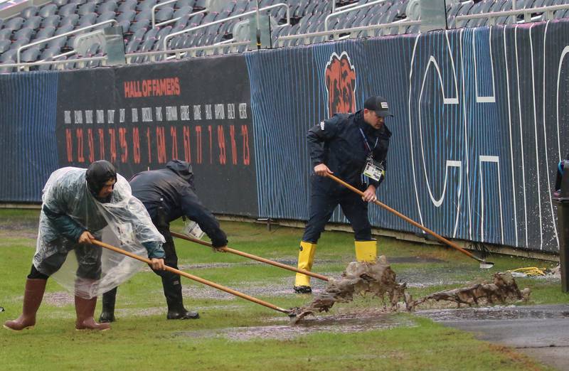 Chicago Bears grounds crew workers use squeegees standing water on the field from the morning rain before the game against the New Orleans Saints on Sunday, Oct .11, 2025 at Soldier Field in Chicago.