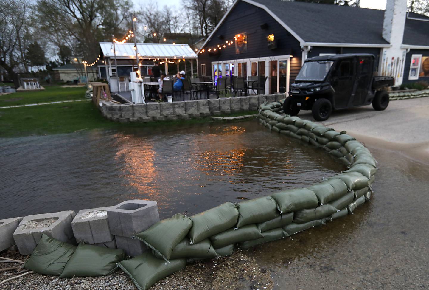 People hang out on the deck of the Bru Crew Bar and Grill as sandbags line the boat ramp area next to the restaurant on Friday, April 17, 2026, in Johnsburg.